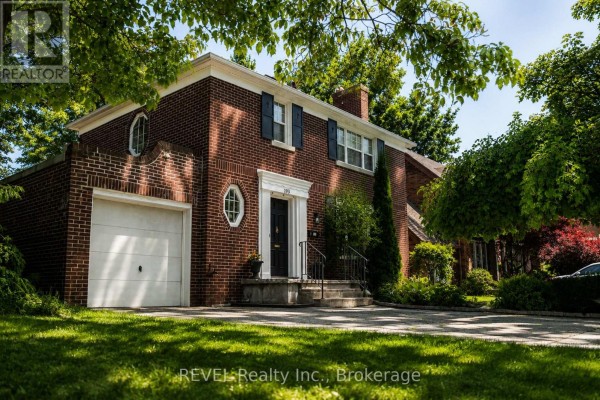 Another front exterior perspective of the house, with sunlight filtering through the trees. - 193 Ontario Street, St  Catharines