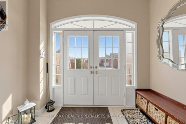 Interior view of a bright entryway with double white doors, sidelights, and a wooden bench. - 193 Queen Mary Drive, Brampton
