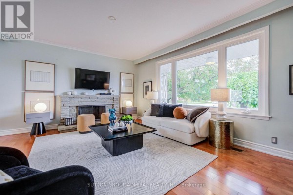 Living room with a stone fireplace, white sofa, large window, and wooden floors. - 193 The Westway, Toronto