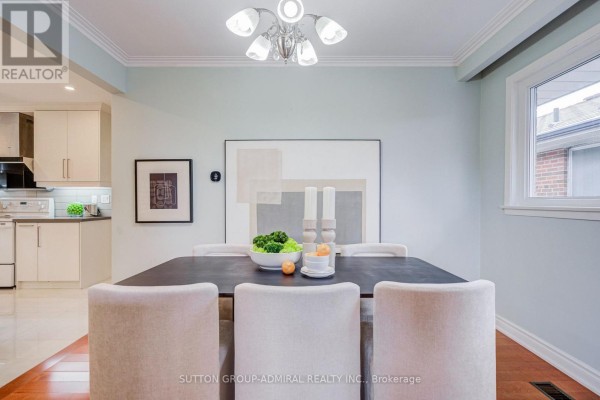 Dining room with a dark table, upholstered chairs, and view of a modern white kitchen. - 193 The Westway, Toronto