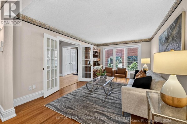 Living room with French doors, a sofa, a glass coffee table, armchairs, and large windows. - 193 Wigwoss Drive, Vaughan