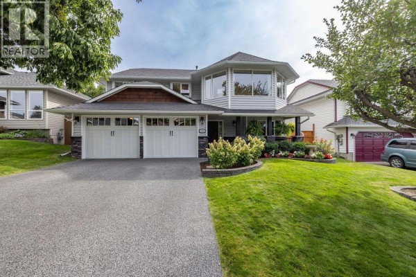 Front view of a grey two-story house with white garage doors and wood trim. Large octagonal window section on the second floor. - 1931 Tinniswood Court, Kamloops