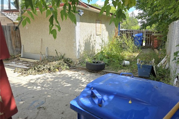 Backyard with a detached garage, two blue garbage bins, and overgrown vegetation. - 1939 Quebec Street, Regina