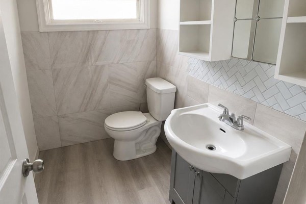 A compact bathroom with a toilet, sink, and vanity against tiled walls. - 1939 Quebec Street, Regina