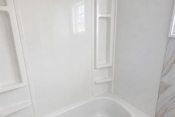 A white bathtub with a grey textured mat and shower curtains, toiletries visible. - 1939 Quebec Street, Regina