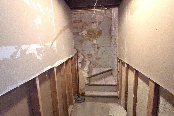 Unfinished basement stairway with exposed wooden studs and concrete floor. - 1939 Quebec Street, Regina