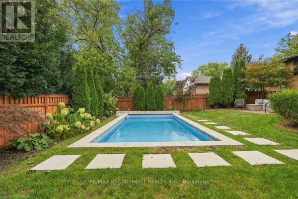 Rectangular swimming pool with white coping and a paved path surrounded by grass and trees. - 194 Foxbar Road, Burlington