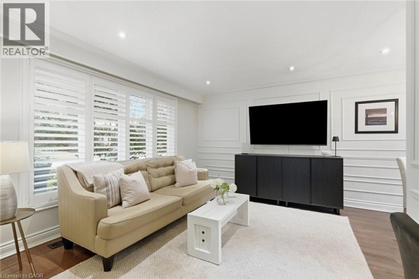 Living room with a beige sofa, white coffee table, large television, and plantation shutters on windows. - 194 Foxbar Road, Burlington