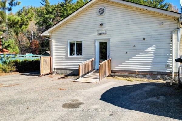 Side exterior of a light-colored building with a wooden ramp leading to a door and a small window. - 194 Hastings Street N, Bancroft