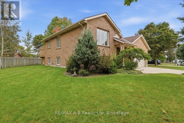 Side view of a brick house with a large green lawn and mature trees. - 194 Norwood Court, Stratford