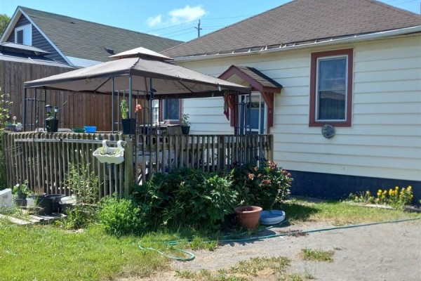 Side and back exterior of a cream-colored bungalow with a wooden deck and gazebo. - 194 Wellington St E, Sault Ste  Marie
