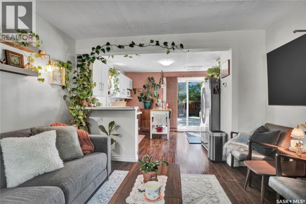 Open concept living area with grey sofa, coffee table, and adjacent white kitchen. - 1940 Coy Avenue, Saskatoon