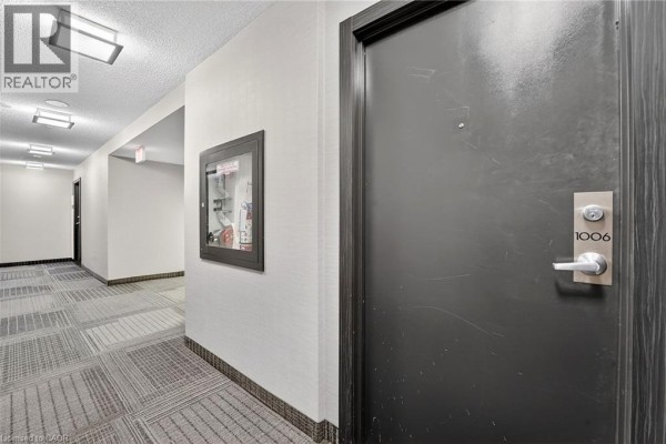 Apartment hallway with a dark grey door labeled 1006 and patterned carpeting. - 1940 Ironstone Drive Unit# 1006, Burlington