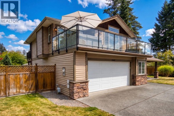 Exterior of a two-story beige house with a large garage door and a second-story balcony. - 1940 Legacy Pl, Nanaimo