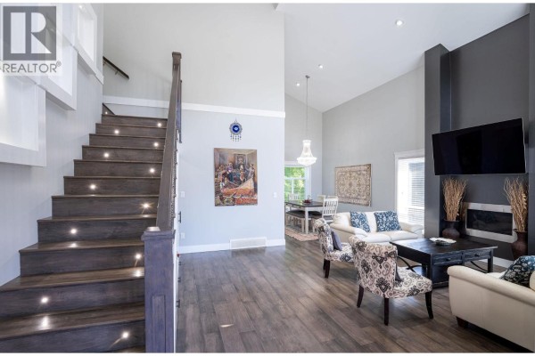 Living room with a dark wood staircase featuring LED lights and a gray and white furniture set. - 1941 Poplar Lane, Revelstoke