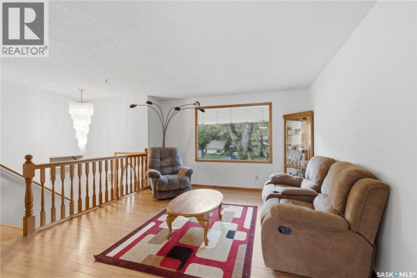 Living room with beige sofa, recliner chair, hardwood floors, and a large window view. - 195 Forsyth Crescent, Regina