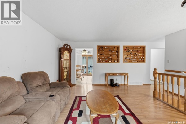 Living room with beige sofa, wood display cabinets, grandfather clock, and a view into the dining room. - 195 Forsyth Crescent, Regina