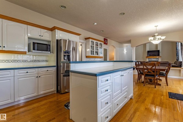 A spacious white kitchen with a large island, stainless steel appliances, and an open view to the dining area. - 195 Kulawy Dr Nw, Edmonton