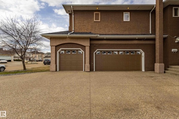 Close-up exterior view of a three-car garage with brown doors and arched window details on a stucco house. - 195 Kulawy Dr Nw, Edmonton