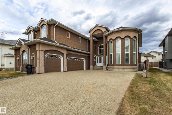 Side view of a large, two-story brown stucco house with multiple garages and arched windows on a cloudy day. - 195 Kulawy Dr Nw, Edmonton