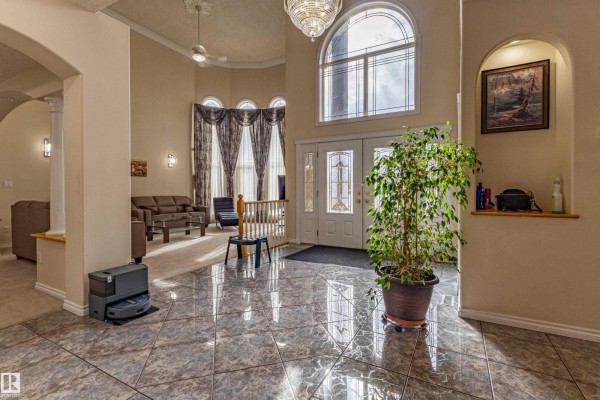 Grand foyer with high ceilings, a chandelier, a large arched window, a potted plant, and tiled floors. - 195 Kulawy Dr Nw, Edmonton