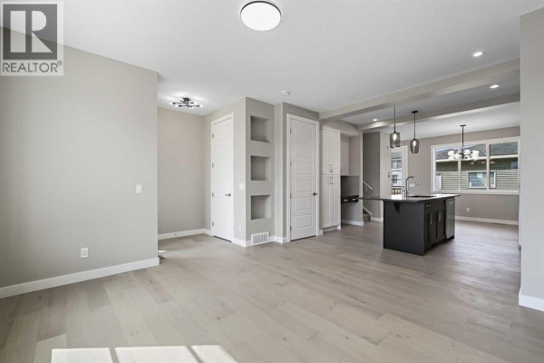 Living room with hardwood floors, a large window, and a dark accent wall with mounted television hookups. - 195 Lanark Gate Se, Airdrie