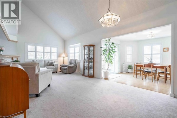 Living room with a vaulted ceiling, beige carpet, two sofas, an armchair, and a display cabinet. - 195 Silverbirch Boulevard, Glanbrook