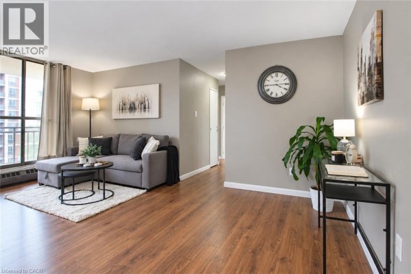Living room with sectional sofa, coffee table, rug, desk, and hallway view. - 1950 Main Street Unit# 705, Hamilton