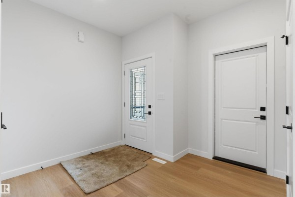 Empty entryway with light wood floors, white walls, a glass-paneled front door, and a rug. - 19503 30 Ave Nw Nw, Edmonton