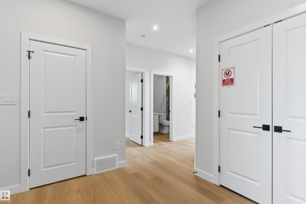 Hallway with light wood floors, white walls, multiple white doors, and a view into a bathroom. - 19503 30 Ave Nw Nw, Edmonton
