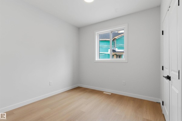 Empty room with light wood floors, white walls, a small window, and a white door. - 19503 30 Ave Nw Nw, Edmonton