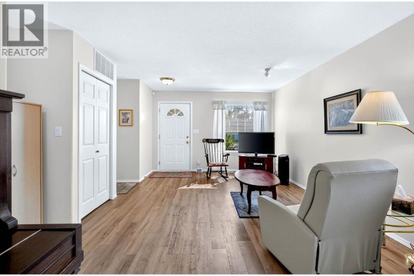 Living room with a recliner, coffee table, and television, showing the entryway. - 1951 Lodgepole Drive Unit# 21, Kamloops