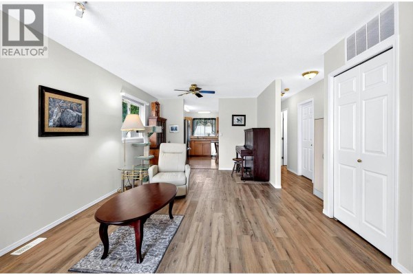 Living room with a recliner, coffee table, piano, and view into the kitchen. - 1951 Lodgepole Drive Unit# 21, Kamloops