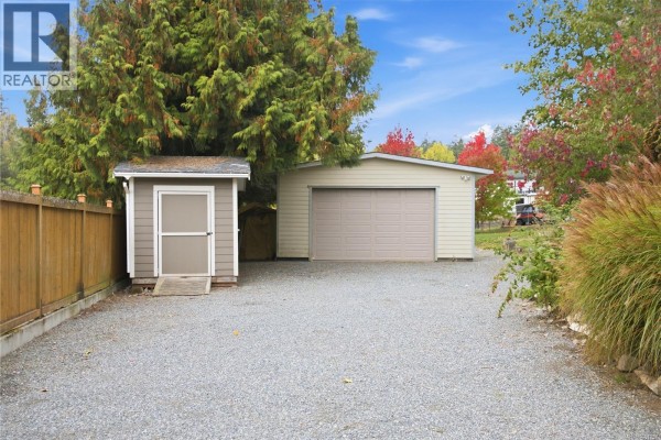 Detached garage and storage shed on a gravel driveway with a wooden fence. - 1951 Szasz Dr, Nanaimo