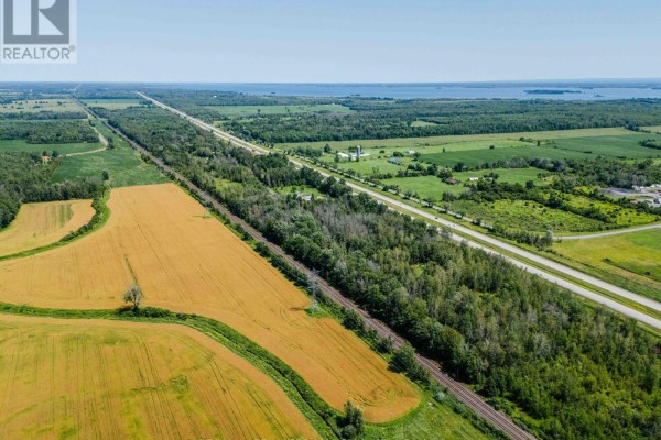 Expansive aerial view of agricultural fields, a highway, railway tracks, and distant water under a cloudy sky. - 19519 Lapierre Road, South Glengarry