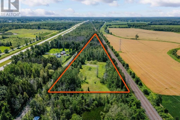 Aerial view of a wooded triangular property parcel outlined in orange, with a clear sky overhead. - 19519 Lapierre Road, South Glengarry