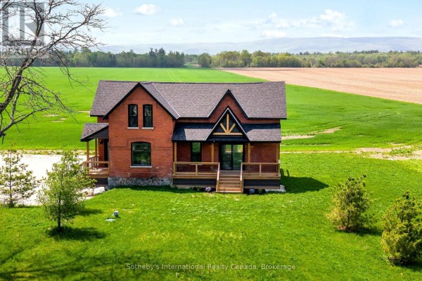 Front view of a red brick house with a dark roof, wooden decks, and large green lawn. - 1952 Nottawasaga Concession 6 N, Clearview