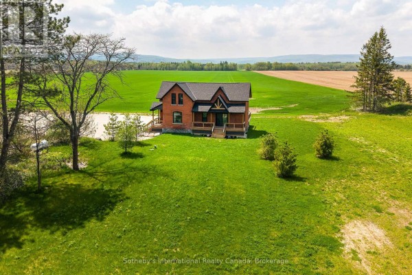 Aerial view of a red brick house with a dark roof, set amidst rolling green fields and trees. - 1952 Nottawasaga Concession 6 N, Clearview