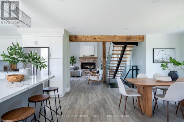 Open-concept living area with a fireplace, wooden beams, stairs, and dining table with chairs. - 1952 Nottawasaga Concession 6 N, Clearview