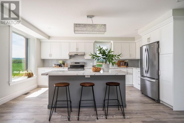 Modern kitchen with white cabinets, stainless steel appliances, an island with seating, and a large window. - 1952 Nottawasaga Concession 6 N, Clearview