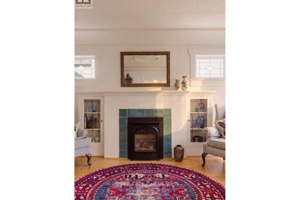 Living room with a fireplace, two armchairs, a wooden cabinet, and a large round rug. - 1955 E 8th Avenue, Vancouver