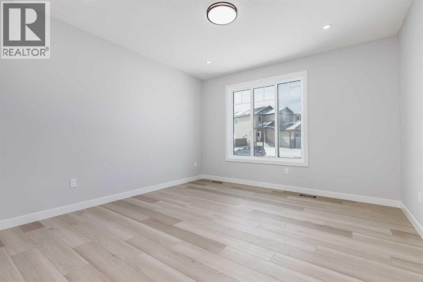 Dining area with light grey walls, light wood floors, and a modern light fixture. - 1955 Mccaskill Drive, Crossfield
