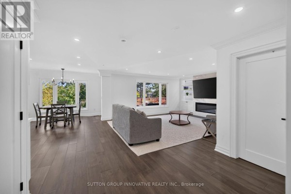 Open concept living and dining area with a fireplace, television, and large windows overlooking greenery. - 196 Bluebell Crescent, Hamilton
