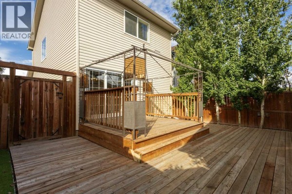 Rear wooden deck and fence of a house, with mature trees visible in the background. - 196 Eversyde Circle Sw, Calgary