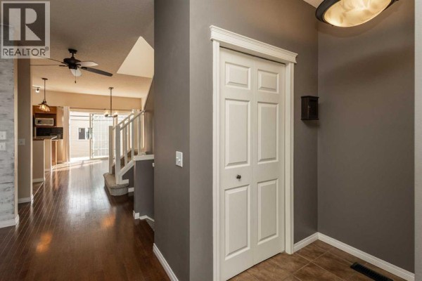 Interior hallway with dark hardwood floors, beige walls, a closet door, and a staircase leading upstairs. - 196 Eversyde Circle Sw, Calgary