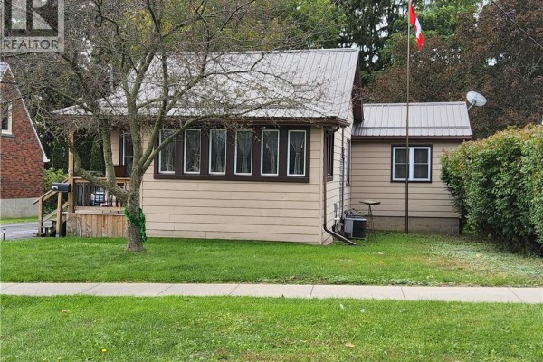 Side exterior view of a light beige bungalow with a detached garage and mature trees. - 196 North Main Street, Simcoe