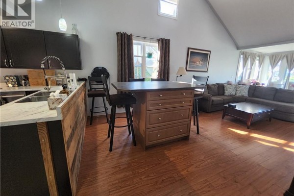 Kitchen island with bar stools, facing a sectional sofa and vaulted ceiling in the living area. - 196 North Main Street, Simcoe