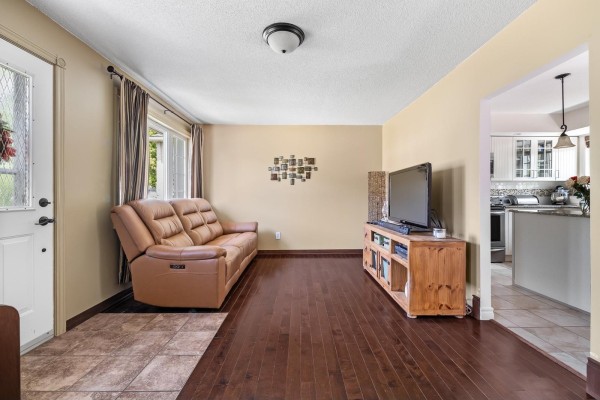 Living room with dark hardwood floors, a tan leather sofa, TV, and a view into the kitchen. - 196 Rue Argyle, Shawville