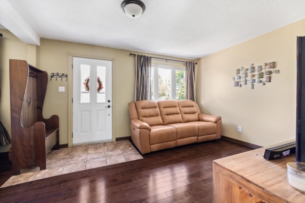 Living room with dark hardwood floors, a tan leather sofa, and a wooden bench by the front door. - 196 Rue Argyle, Shawville