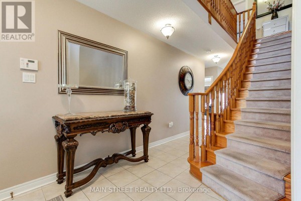 Foyer with tiled floors, a console table, large mirror, and a staircase with wooden banister. - 196 Wainscot Avenue, Newmarket